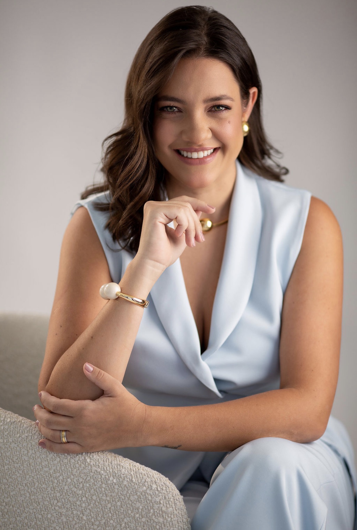 Dra. Nayara Curti, neurologista especializada em cognição e comportamento, sentada e sorrindo com naturalidade em traje azul claro.